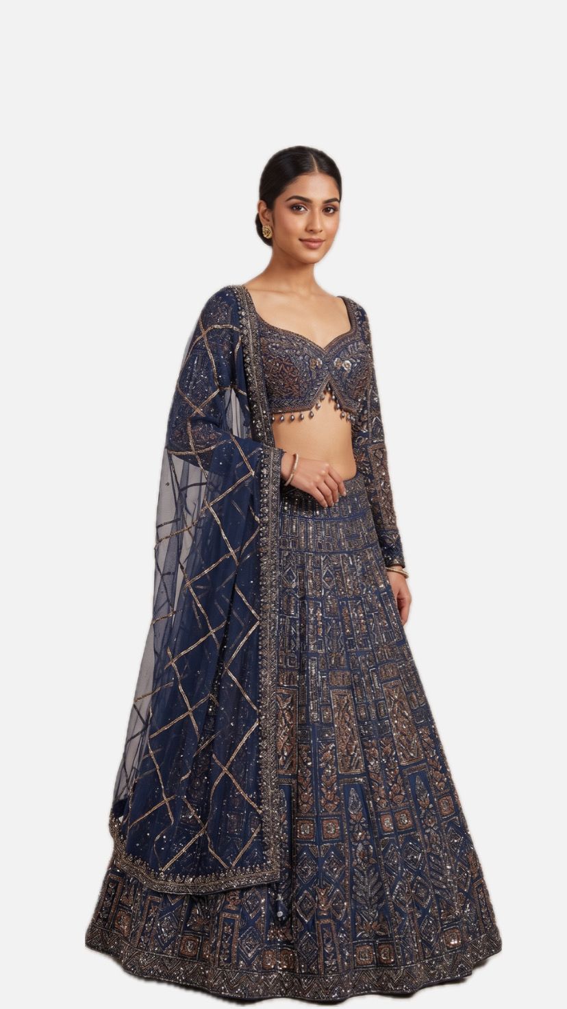 A Yashwanti London women's bridal lehenga choli in a deep navy-blue base, detailed with antique copper and gold embroidery in geometric and floral motifs accented with sequins and bead work. The fitted choli has a sweetheart neckline, full sleeves, and a deep open back fastened with a tie-up dori and beaded latkan drops. The flared A-line skirt carries dense panelled embroidery that builds into a broad ornamental hem, paired with a sheer net dupatta finished in diamond-lattice gota detailing.